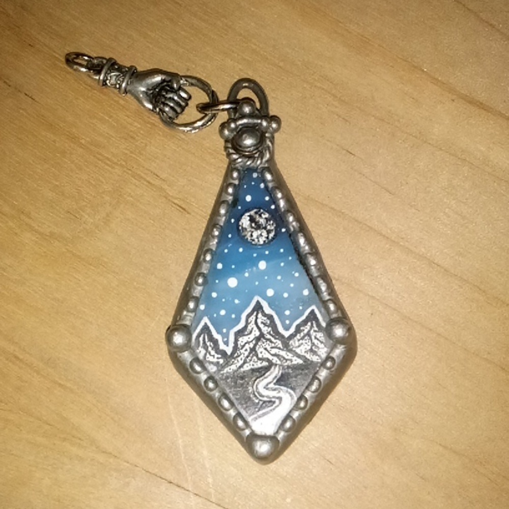 Metal pendant with mountain and sky artwork on resin